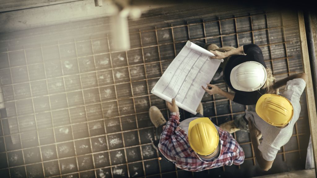 Architect, foreman and engineer on a construction site, looking down on a blueprint.